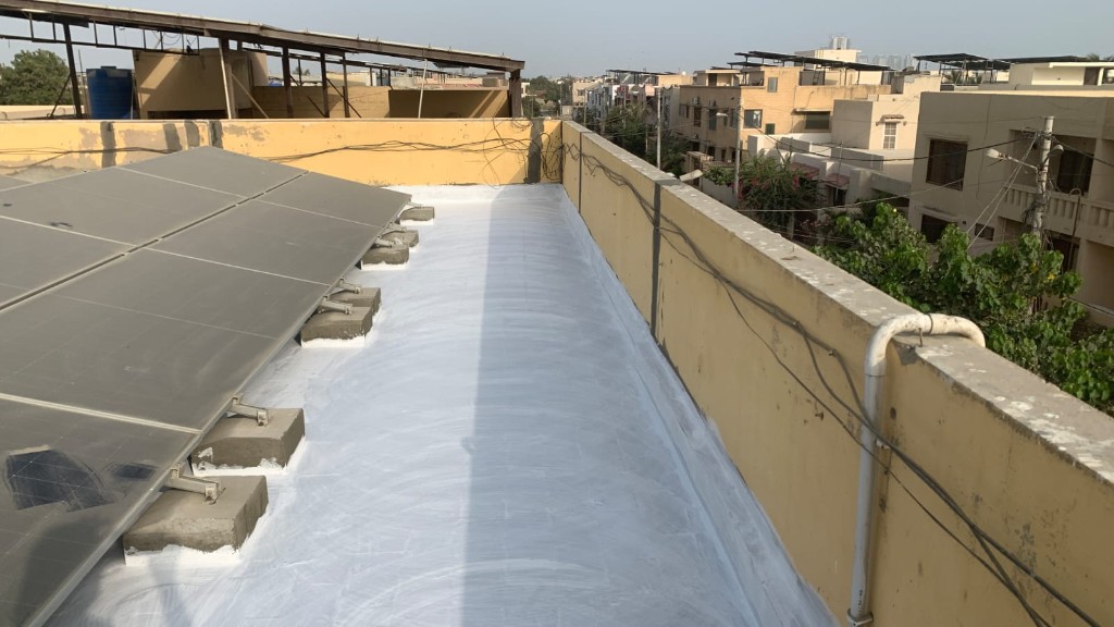 Large grey waterproofed industrial roof with Karachi skyline in background